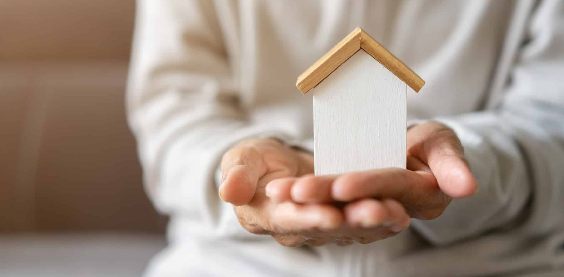 Hände halten schützend kleines Holzhaus | Immobilienfinanzierung Krefeld